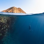 a person swimming in the ocean with a mountain in the background